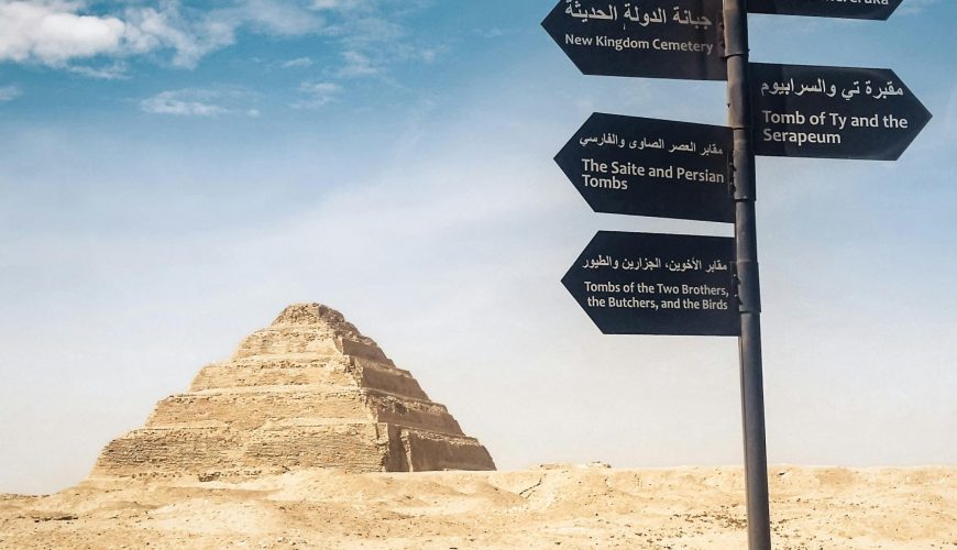 Signpost near the Pyramid of Djoser in the Egyptian desert, clear blue sky.