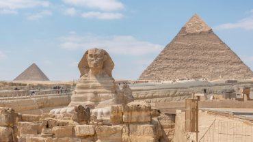 Iconic view of the Great Sphinx and Giza Pyramids in Egypt under a clear blue sky.