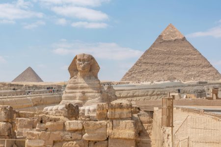 Iconic view of the Great Sphinx and Giza Pyramids in Egypt under a clear blue sky.