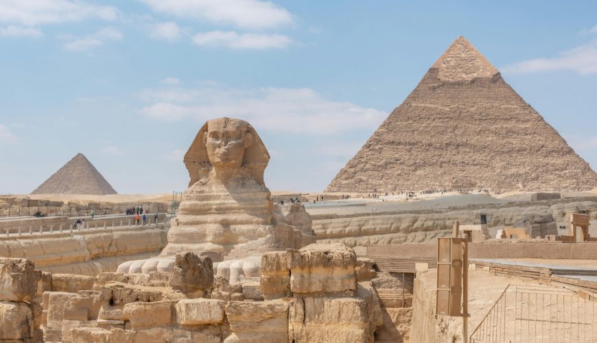 Iconic view of the Great Sphinx and Giza Pyramids in Egypt under a clear blue sky.