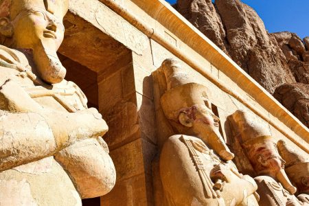 Ancient Egyptian statues at Hatshepsut Temple in Luxor under a clear blue sky.