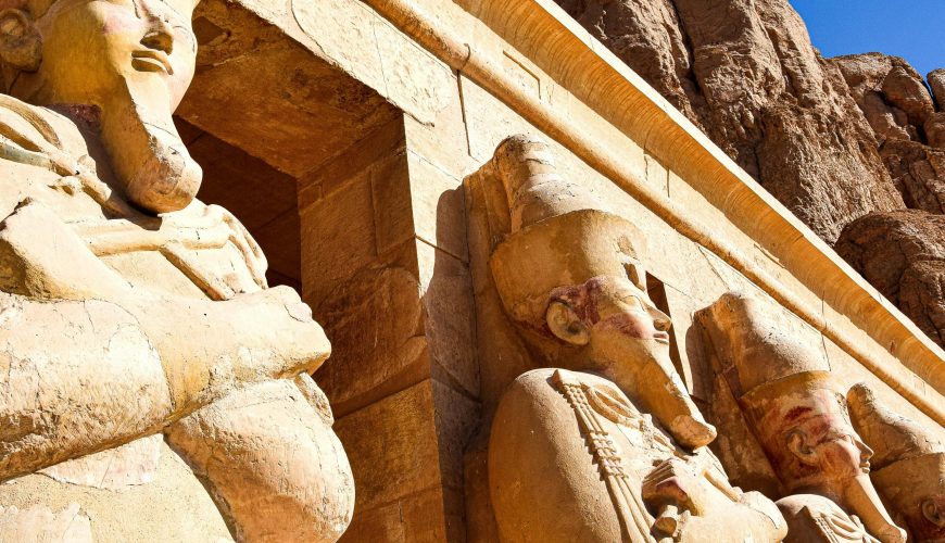 Ancient Egyptian statues at Hatshepsut Temple in Luxor under a clear blue sky.