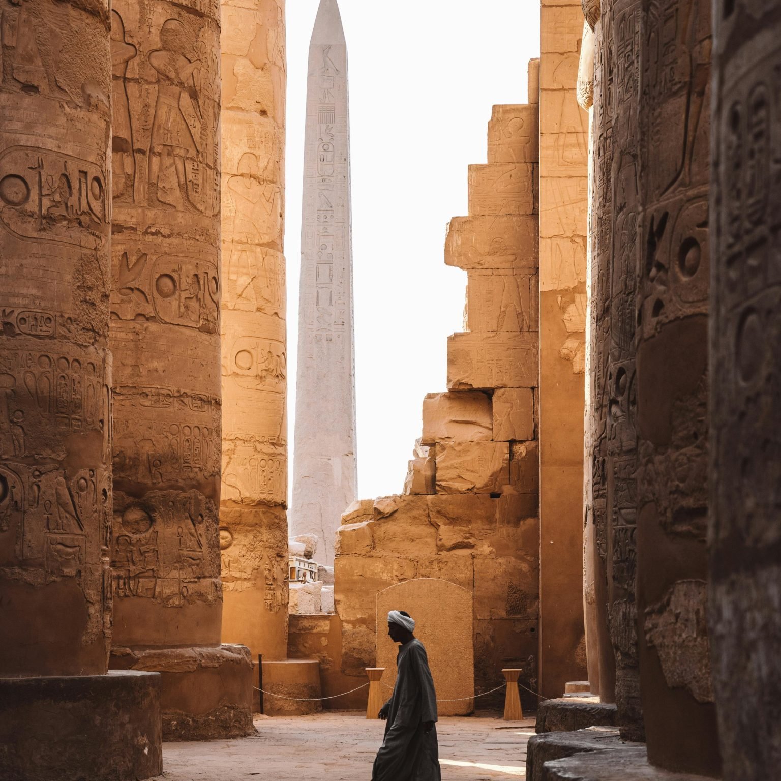 A serene view of the Karnak Temple's ancient columns and obelisk with a person walking through.
