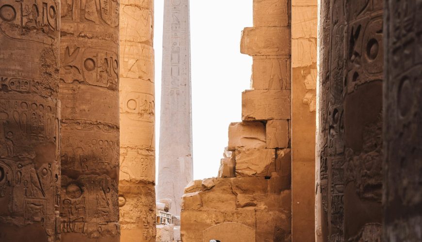 A serene view of the Karnak Temple's ancient columns and obelisk with a person walking through.