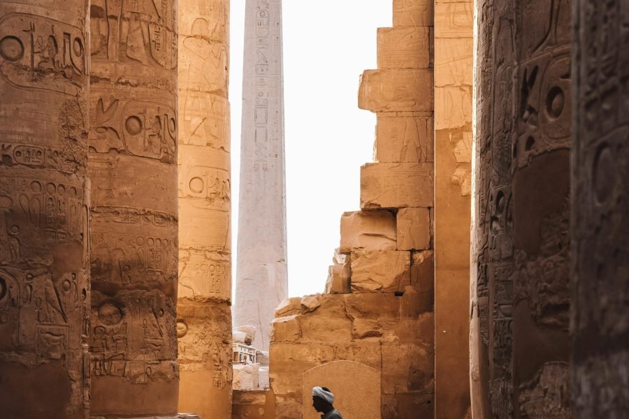 A serene view of the Karnak Temple's ancient columns and obelisk with a person walking through.