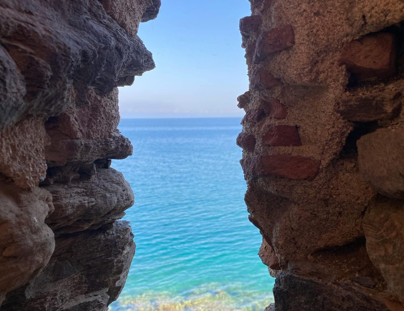 Captured through a stone wall, a mesmerizing view of the clear blue ocean and horizon.