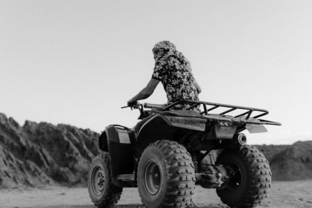 A person rides an ATV in a rugged desert terrain, captured in dramatic black and white.