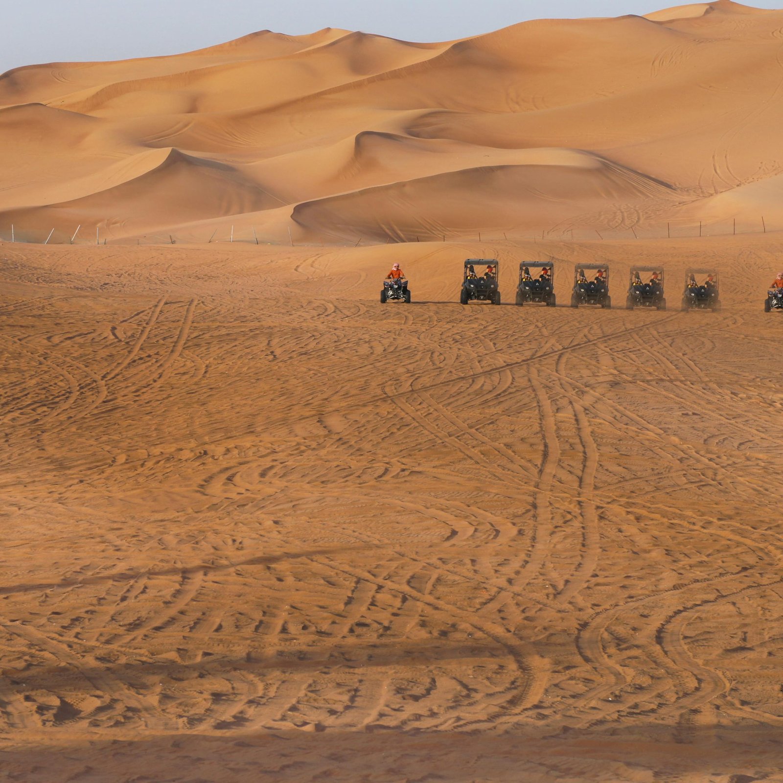 Group of ATVs navigating vast sand dunes under clear sky.