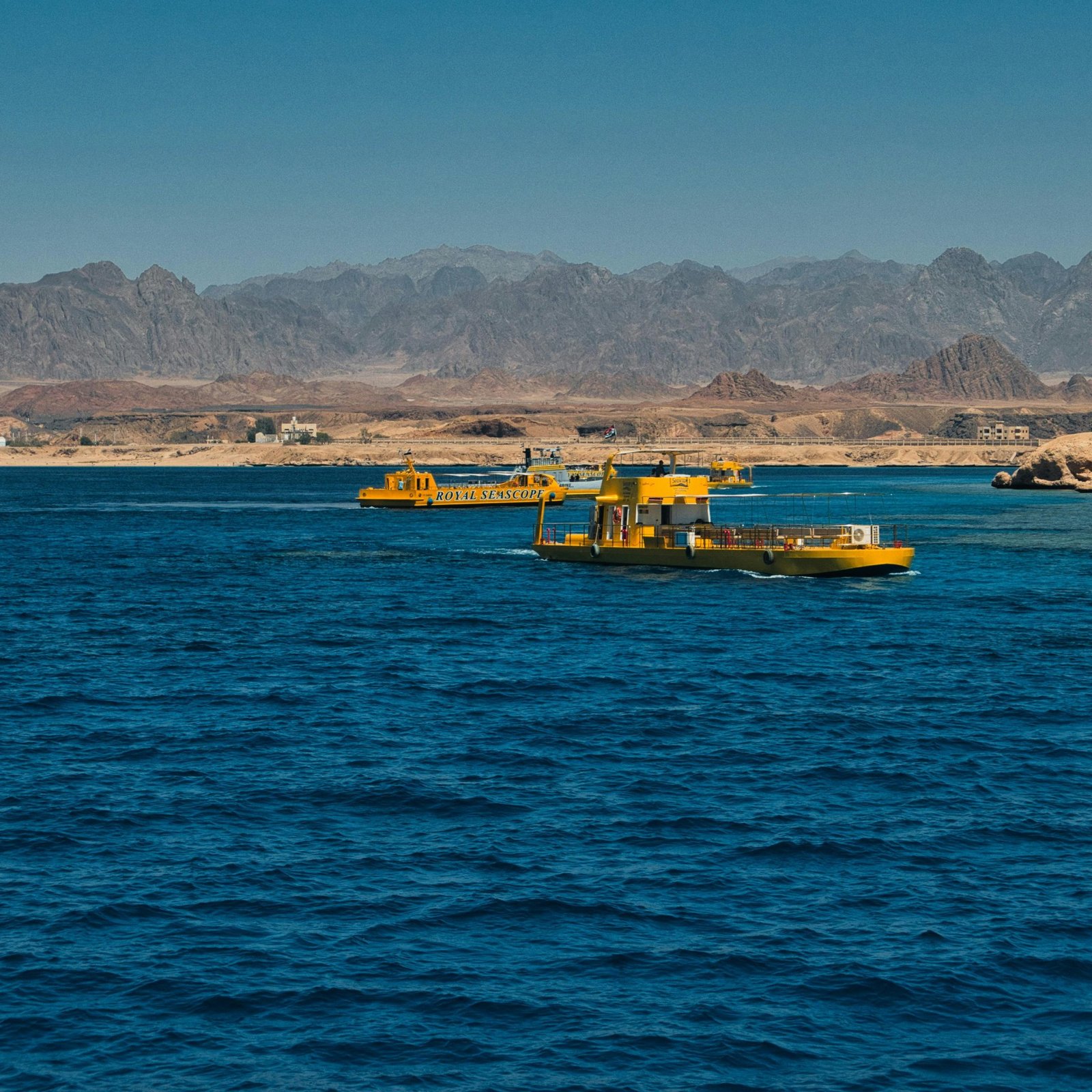 Yellow boats float on the vibrant blue waters of Ras Mohammed with scenic Egyptian mountains in the background.